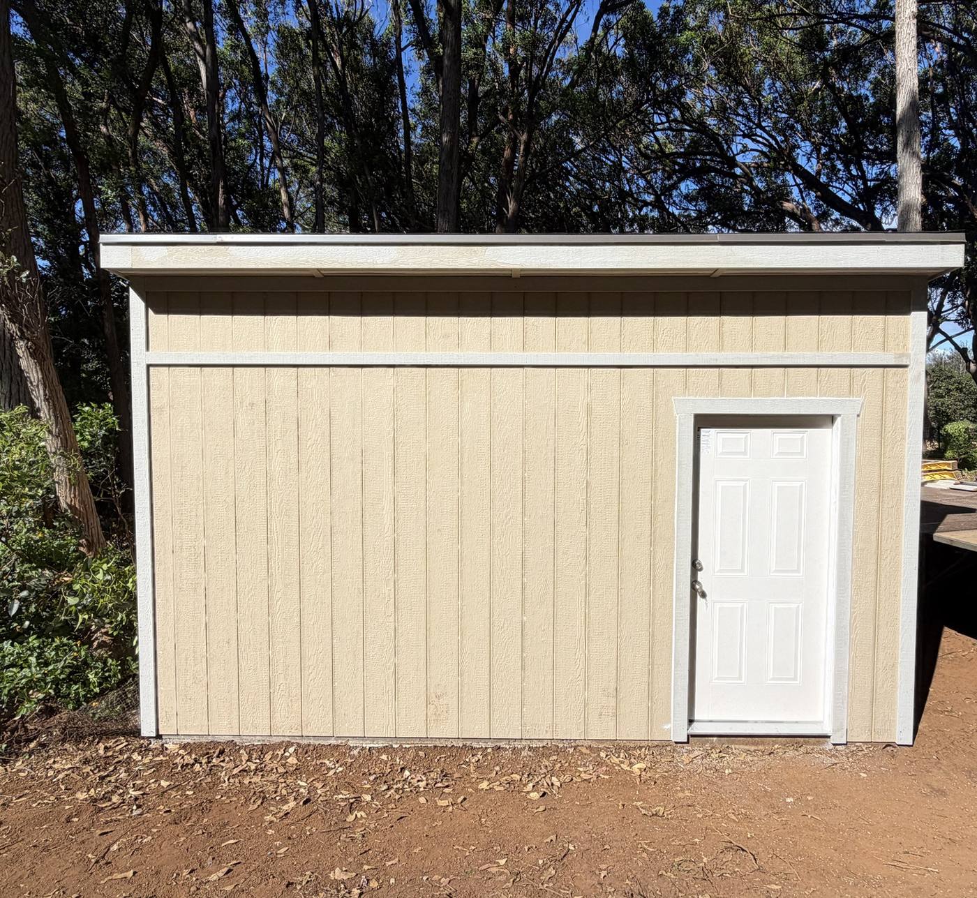 Tan lean-to shed with a white entry door