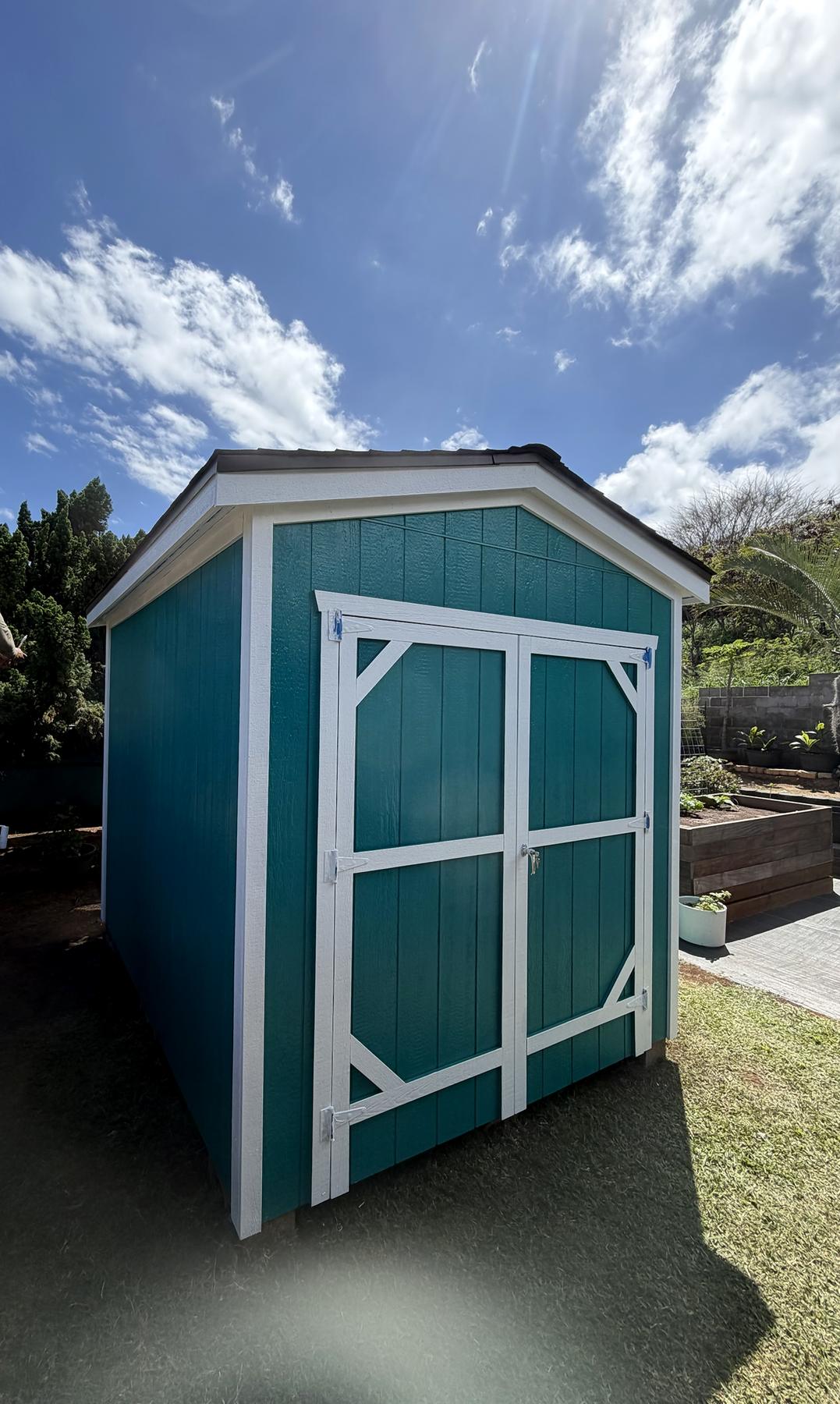 Teal shed with white trim and double barn doors beside garden beds